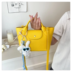 Detailed shot of yellow mini leather tote bag with cute plush bunny charm and crossbody strap