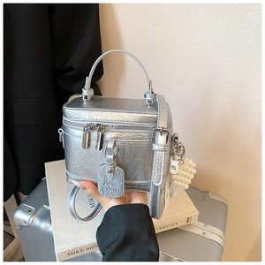 Detailed shot of a silver pleated box handbag with a pearl charm and metal zippers