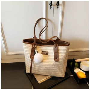 Detail of straw tote bag showing natural weave texture, brown leather handles and pompom