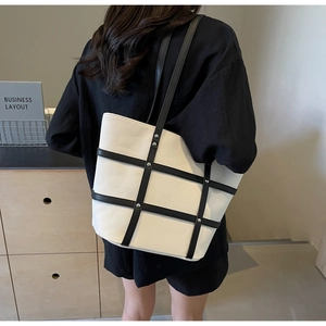 Detail of white canvas tote bag with black leather grid and rivets on model