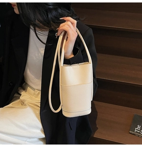 Minimalist white litchi pattern leather bucket bag shown held by a seated model