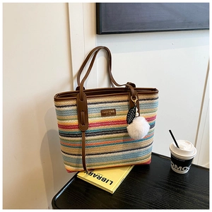 Detail of colorful striped woven tote bag with brown leather handles and leaf charm