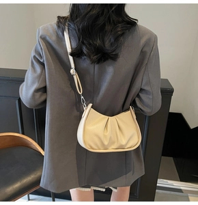 Model view of beige pleated cloud bag with adjustable silver buckle strap on grey blazer
