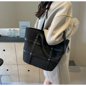 Close-up of black tote bag with silver rivets and leather straps worn by a model