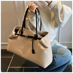 Close-up of beige canvas tote bag showing black leather handles and gold D-ring buckle