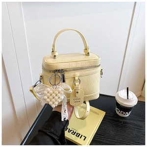 Close-up of a pale yellow box bag featuring a pearl heart lace charm and retro texture