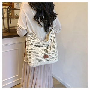 Detail of hollow woven shoulder bag with brown leather patch and slim strap in ivory