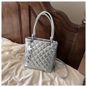 Détail du sac cabas argenté matelassé avec breloques étoiles sur un drap blanc
