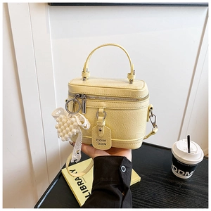 Detail of light yellow leather box bag with dual zippers, pearl charm and thin strap