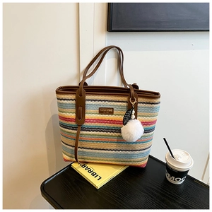 Detail of colorful woven straw tote with brown leather handles and a white pompom charm