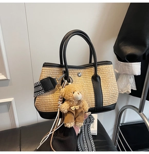 Détail du sac seau en paille avec garniture en cuir noir, bandoulière et ourson