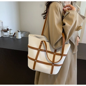 Detail of canvas tote bag with brown leather straps and silver metal studs in a cafe setting