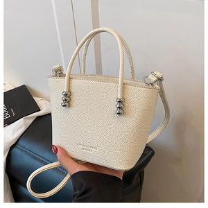 Close-up of cream crossbody bucket bag featuring silver bead handles and litchi texture