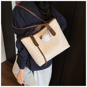 Detail of bohemian woven straw tote bag with brown leather straps and plush charm
