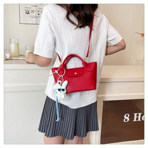 Detail of red mini tote bag with white bunny plush charm worn by a model in a cafe