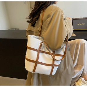 Detail of white canvas bucket bag featuring brown leather cage straps and metal studs