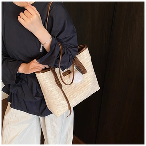 Detail view of woven straw tote bag featuring brown leather trim and plush pompom charm