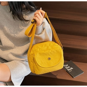 Details einer gelben Nylon-Umhängetasche mit rundem Metalllogo und verstellbarem Gurt