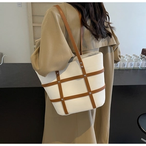 Detail view of large white tote bag with brown leather lattice and silver metal rivets