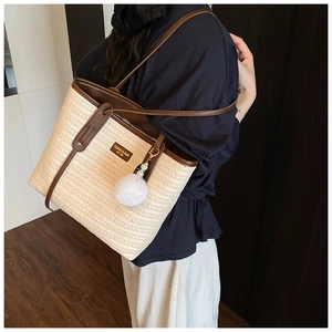 Detail of bohemian straw tote bag with brown leather trim and fluffy pompom decoration