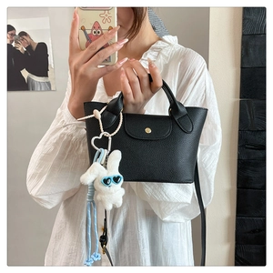 Detail of black lychee grain mini tote bag with gold buckle and white bunny charm