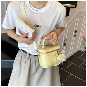 Detail view of yellow box-shaped handbag with pearl charm and lace accent on textured leather