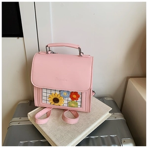 Detailed close-up of pink PU leather backpack with sunflower embroidery on a silver suitcase