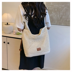 Close-up of cream crochet tote bag with brown leather strap and decorative logo patch