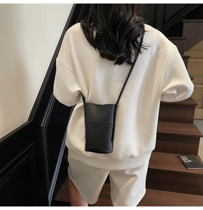 Detail of minimalist black pebbled leather crossbody phone bag on model at staircase