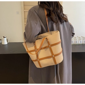 Detail of canvas and brown leather tote bag with rivet studs worn on model's shoulder
