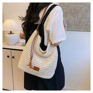 Detail of a beige crochet tote bag featuring brown leather straps on a model back