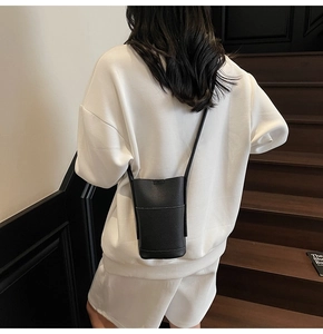 Detail of black pebbled leather crossbody phone bag on model showing minimalist vertical design