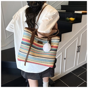 Detail of colorful striped woven tote bag with brown leather handles and pom-pom charm