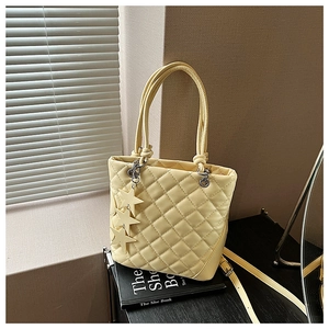 Détail d'un sac cabas matelassé jaune clair avec breloques étoiles posé sur un livre