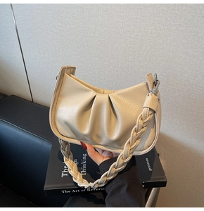 Detail of cream pleated cloud bag featuring a thick braided shoulder strap on black books