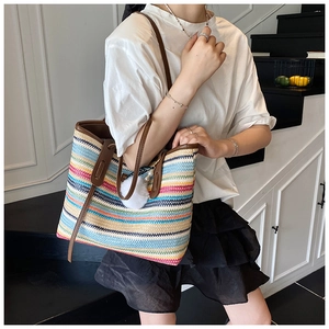 Detail of colorful striped straw tote bag with brown leather straps and pompom charm