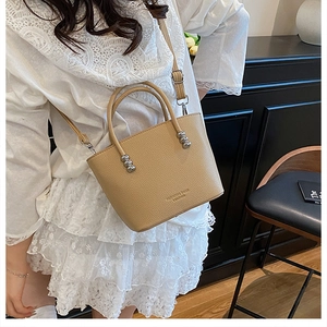 Close-up of beige lychee grain leather handbag with silver metallic bead decor and strap