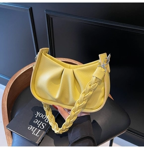 Detail of yellow pleated cloud bag featuring a chunky hand-woven handle on leather chair