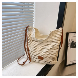 Detail of cream woven tote bag featuring a leather patch and adjustable brown strap