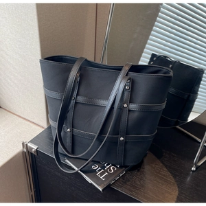 Detail of black canvas tote bag showing leather straps and silver rivet accents