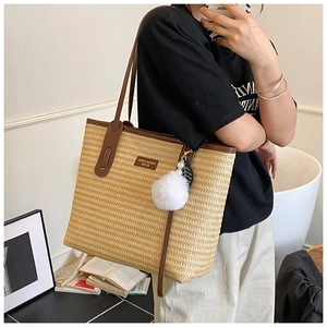 Detail of bohemian straw tote bag featuring brown leather handles and plush charm accessory