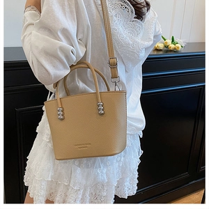 Detail of beige leather handbag with silver bead accents and engraved brand text on the body