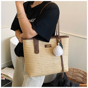 Detail of large straw tote bag with brown leather trim and decorative tassel charms