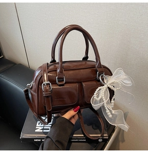 Detail of brown Boston bag with oil wax leather finish and mesh pearl bow charm