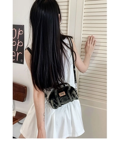 Vue détaillée du mini sac cylindre en jean rétro avec écusson orange porté en bandoulière