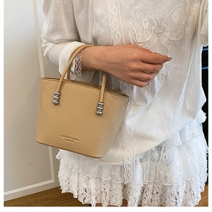 Detail of beige lychee leather handbag with silver beaded handle and printed logo texture