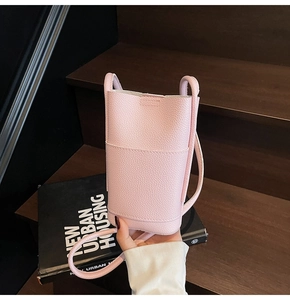 Pink lychee-textured leather crossbody phone bag with front pocket held by hand