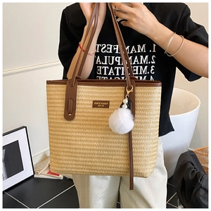 Detailed view of bohemian straw tote bag with brown leather handles and plush charm