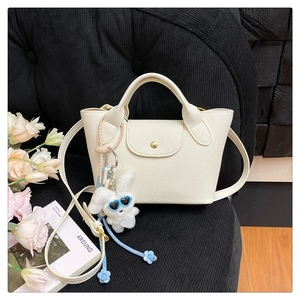 Detail of white lychee leather tote bag with gold snap and cute bunny keychain charm