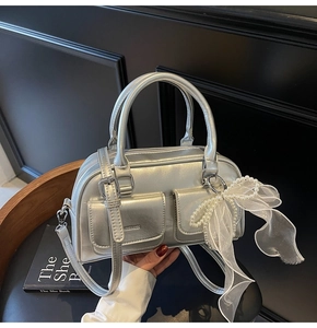 Close-up of metallic silver Boston bag with pearl bow charm and dual handle details
